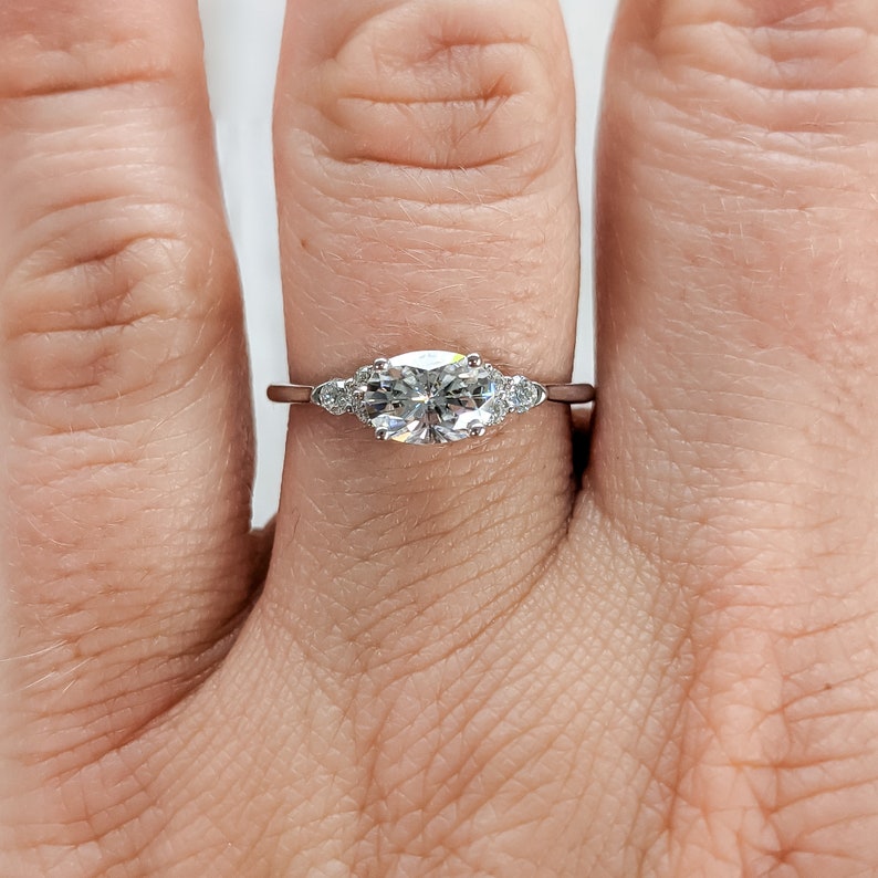 May include: A silver ring with a large oval-shaped center stone and two smaller round stones on either side.