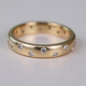 Può includere: Un anello a fascia in oro con finitura spazzolata e piccoli diamanti rotondi incastonati nella fascia.