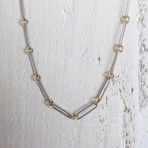 May include: A silver chain necklace with gold accents. The chain is made of interlocking oval links.