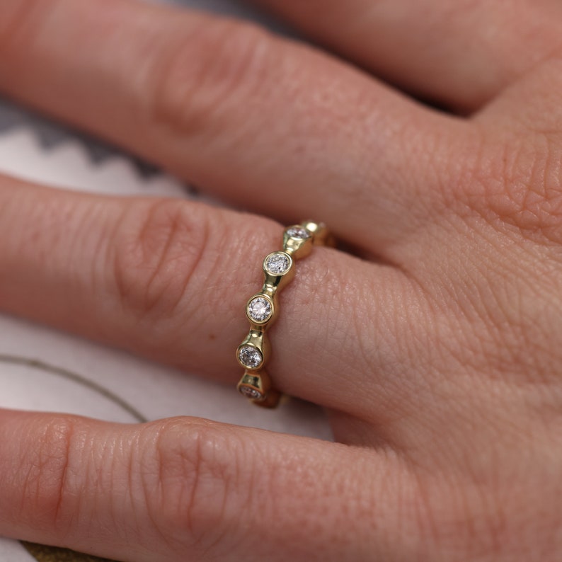 May include: A gold band ring with a row of round diamonds set in a bezel setting.