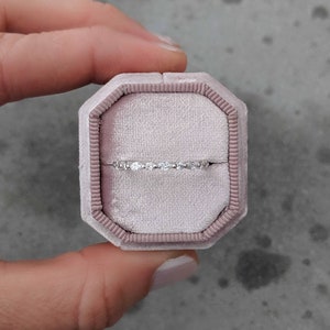 May include: A delicate diamond ring in a pale pink velvet ring box. The ring features a row of small, round diamonds set in a thin band.