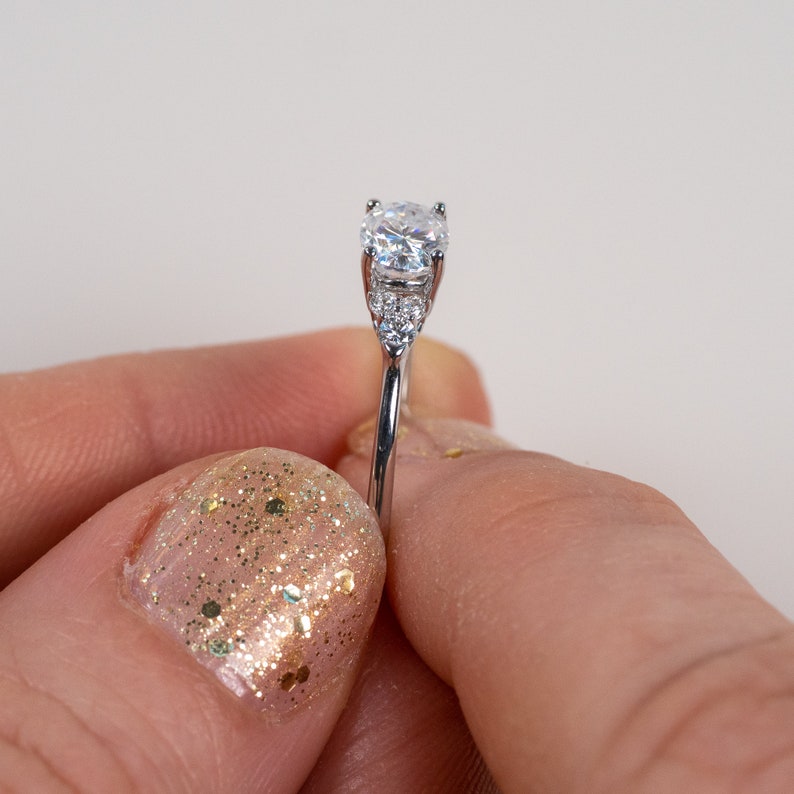 May include: A silver ring with a large, clear, round-cut center stone and smaller, clear, round-cut accent stones on the band.