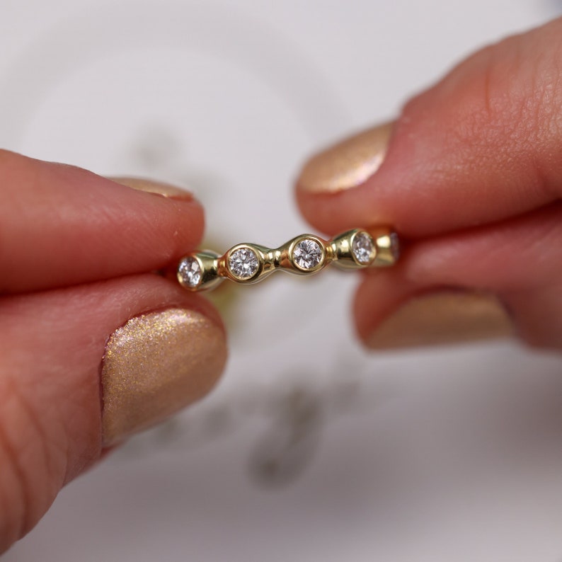 May include: A gold band ring with five round diamonds set in a wavy pattern.