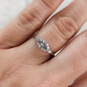 May include: A silver ring with an oval-shaped center stone and two smaller accent stones on either side.