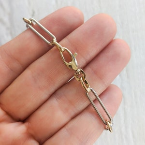 May include: A gold and silver chain bracelet with a lobster clasp closure. The chain is made of interlocking oval links.