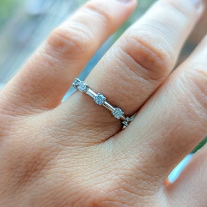 May include: A silver band ring with five small, clear gemstones set in a row.