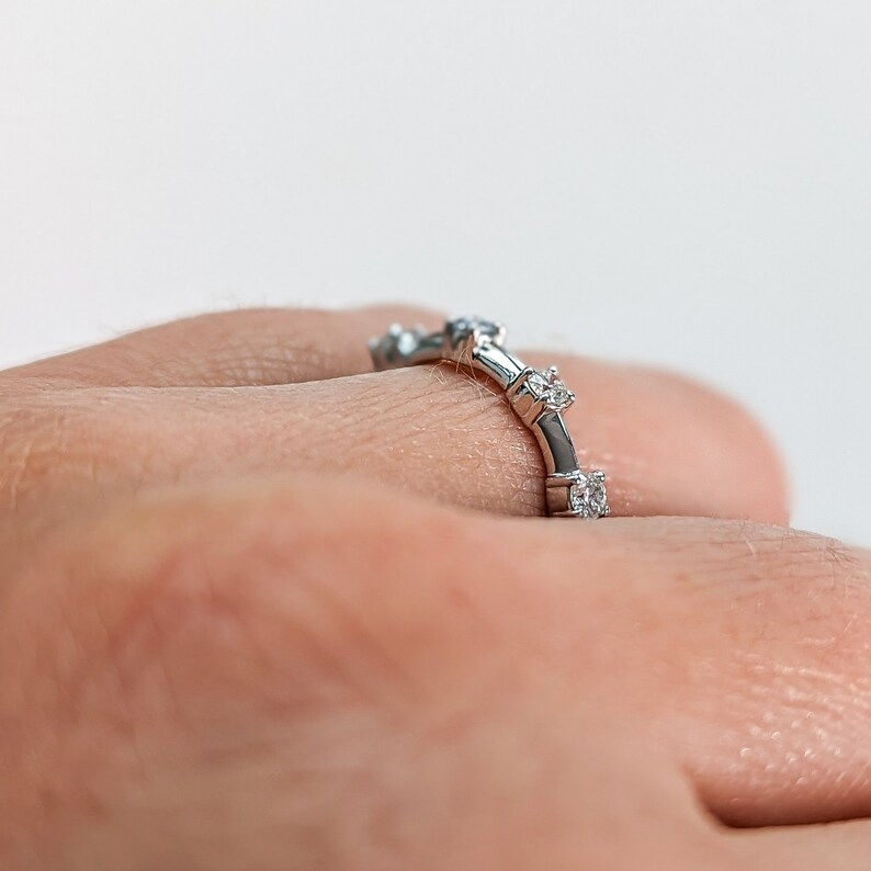 May include: A silver band ring with small diamonds set in the band. The ring is on a person's finger.