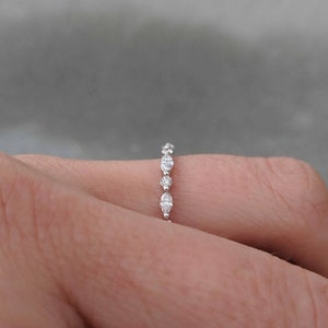 May include: A delicate silver band ring with a row of small, round, and oval-shaped clear gemstones.