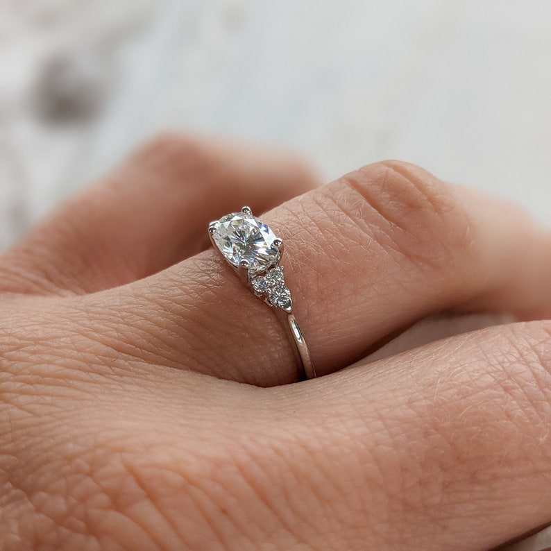 May include: A silver engagement ring with a large oval-shaped center stone and three smaller round stones on the band.