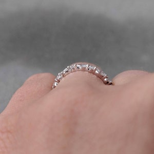 May include: A silver band ring with a row of small, clear, round-shaped stones.