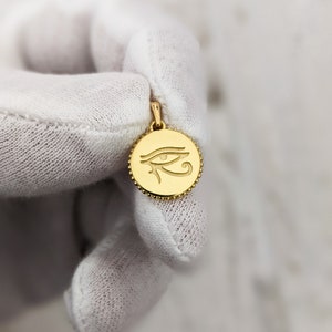 May include: A gold pendant with a detailed engraving of the Eye of Horus, a symbol of protection and good health in ancient Egyptian mythology.