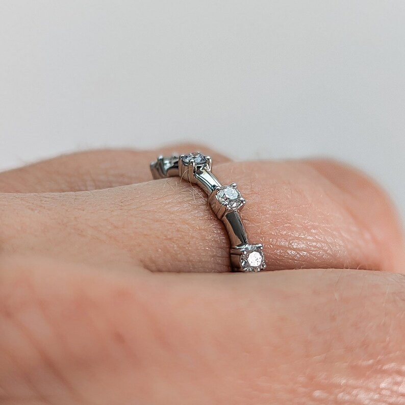May include: A silver band ring with five small, clear gemstones set in a curved line.