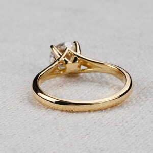 May include: A gold solitaire engagement ring with a round-cut diamond. The ring features a classic four-prong setting and a polished gold band. The diamond is the focal point, set high to maximize light reflection.