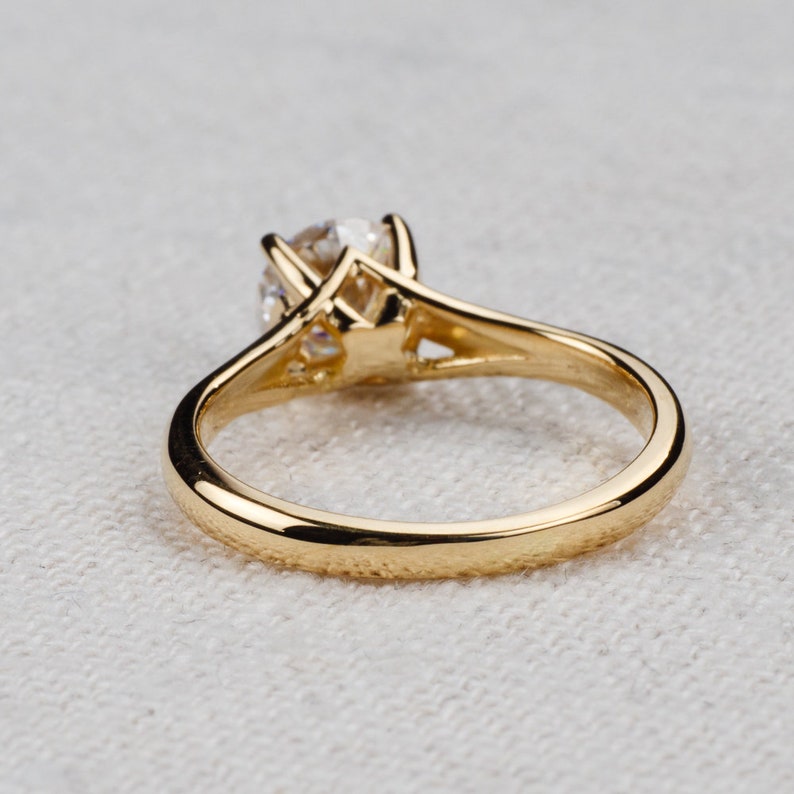 May include: A gold solitaire engagement ring with a round-cut diamond. The ring features a classic four-prong setting and a polished gold band. The diamond is the focal point, set high to maximize light reflection.