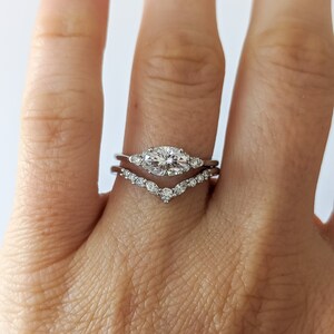 May include: A close-up of a hand wearing two silver rings with small diamonds. The top ring features a larger oval-shaped diamond in the center.