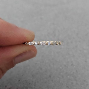 May include: A delicate gold band ring with a row of small, round, and oval-shaped diamonds.