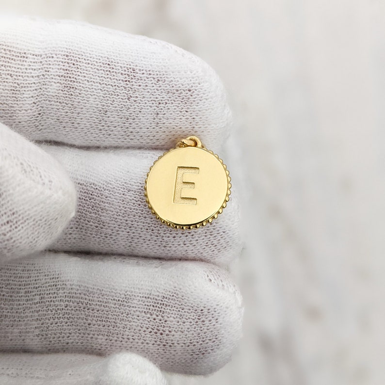 May include: Gold-toned pendant charm with a raised letter 'E' in the center. The charm is round and has a beaded edge.