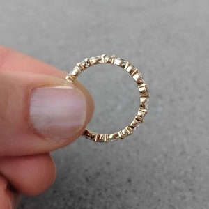 May include: A gold band ring with a row of small, clear gemstones set in a pave setting.