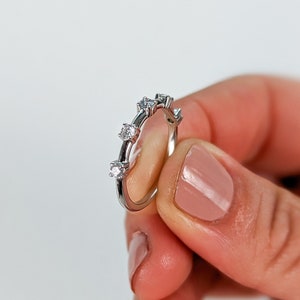 May include: A silver ring with five small clear stones set in a row around the band.