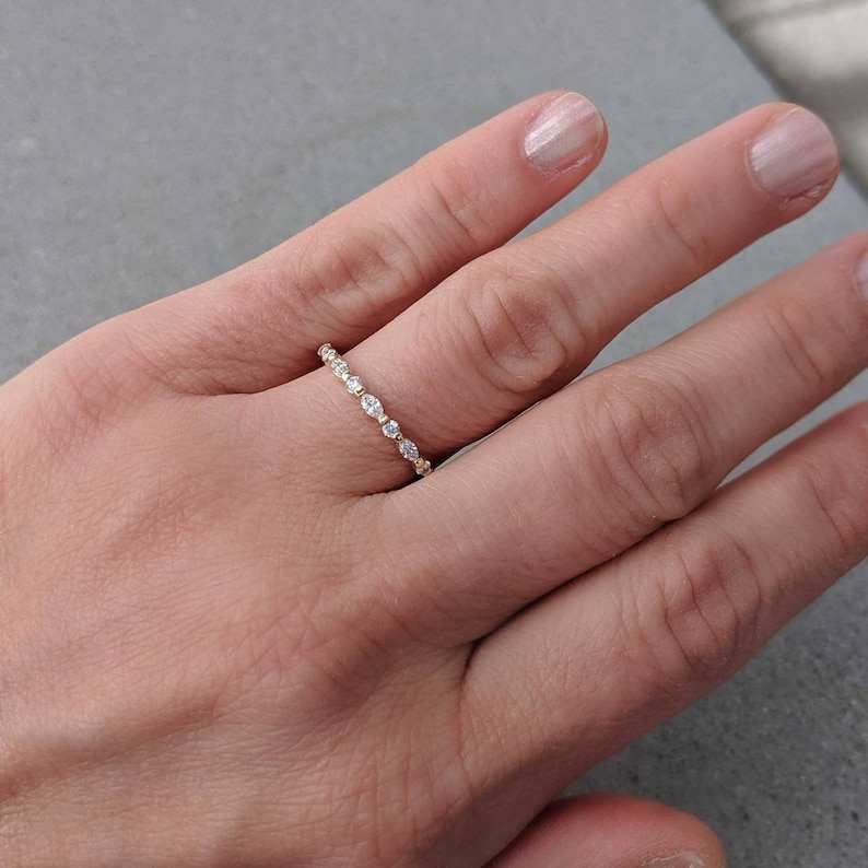 May include: A delicate gold band with a row of small, clear gemstones. The ring is worn on a person's finger.