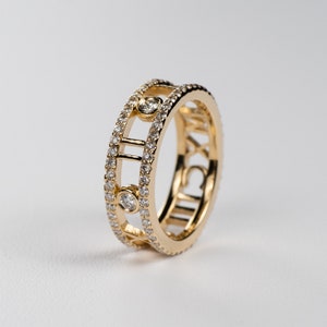 May include: A gold band ring with a row of small diamonds and the Roman numeral 'XII' on the side. The ring has a design of a circle with a line through the center.