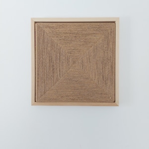 Könnte beinhalten: Quadratische Kunst mit einem gewebten Design in Brauntönen, eingefasst in einem hellen Holzrahmen. Das Kunstwerk weist ein geometrisches Muster auf, das den Blick in die Mitte lenkt. Dieses Stück ist eine einzigartige Wanddekoration.