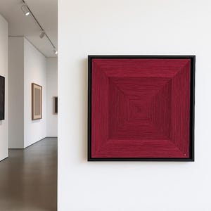 Könnte beinhalten: Ein gerahmtes Kunstwerk mit einem geometrischen Design. Das Kunstwerk ist ein Quadrat aus konzentrischen Quadraten in tiefroter Farbe, mit einem schwarzen Rahmen. Es wird an einer weißen Wand in einer Galerie gezeigt.