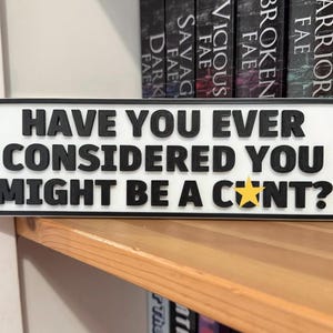 Könnte beinhalten: Ein rechteckiges weißes Schild mit schwarzem Rand und erhabener schwarzer Schrift, auf dem steht: HAVE YOU EVER CONSIDERED YOU MIGHT BE A C*NT? Der Buchstabe U im letzten Wort ist durch einen kleinen, gelben fünfzackigen Stern ersetzt.