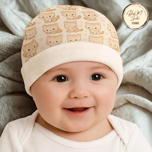 May include: A baby wearing a beige beanie hat patterned with cartoon kittens. The hat has a cream-coloured brim. The baby is wearing a white onesie and smiling. The background is a soft, neutral-toned blanket.