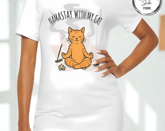 May include: White t-shirt featuring a cartoon orange tabby cat in a yoga pose, with the text "NAMASTAY WITH MY CAT". The design includes a lotus flower and incense smoke. A round logo with the text "Honey M. Dote Studios" is in the upper right corner.