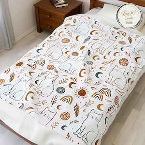 May include: White blanket with a repeating pattern of stylized cats, rainbows, moons, suns, and leaves in brown, green, and gold. The blanket is on a bed with a wooden frame and a nightstand.