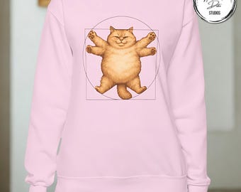 Puede incluir: Sudadera rosa claro con un gato de dibujos animados en la pose del Hombre de Vitruvio. El gato marrón está representado dentro de un círculo y un cuadrado. La sudadera es de color rosa claro liso.