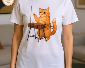 May include: White t-shirt featuring a whimsical illustration of an orange tabby cat playing a theremin. The cat is depicted with its paw raised, interacting with the instrument. The design is printed on a classic crew neck tee.