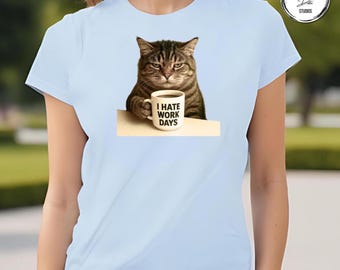 May include: Light blue t-shirt featuring a grumpy cat holding a coffee mug. The mug has the text "I HATE WORK DAYS" printed on it. The cat is brown and gray with a displeased expression.