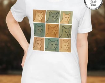 May include: White t-shirt with a grid of nine cat portraits in different colours. Each square displays a cat illustration in shades of beige, green, and brown. The shirt has a crew neck and short sleeves.