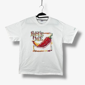 Può includere: T-shirt bianca con una grafica di un peperoncino rosso all'interno di una cornice colorata. Il testo "Bite Me" è sopra il peperoncino. La maglietta è appesa a una gruccia nera.