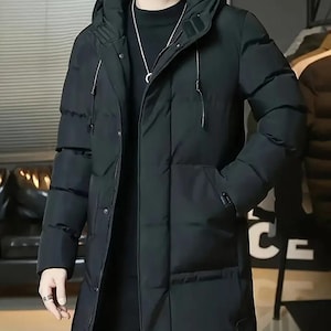 May include: A black, hooded winter coat with a longline design. The coat features a zipper closure, multiple pockets, and a drawstring hood. The coat is made of a quilted material and is designed to provide warmth and protection from the elements.