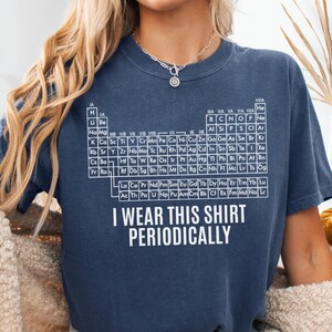 May include: A navy blue t-shirt with a white periodic table design and the text "I WEAR THIS SHIRT PERIODICALLY." The shirt is a comfortable, casual style, perfect for science enthusiasts.