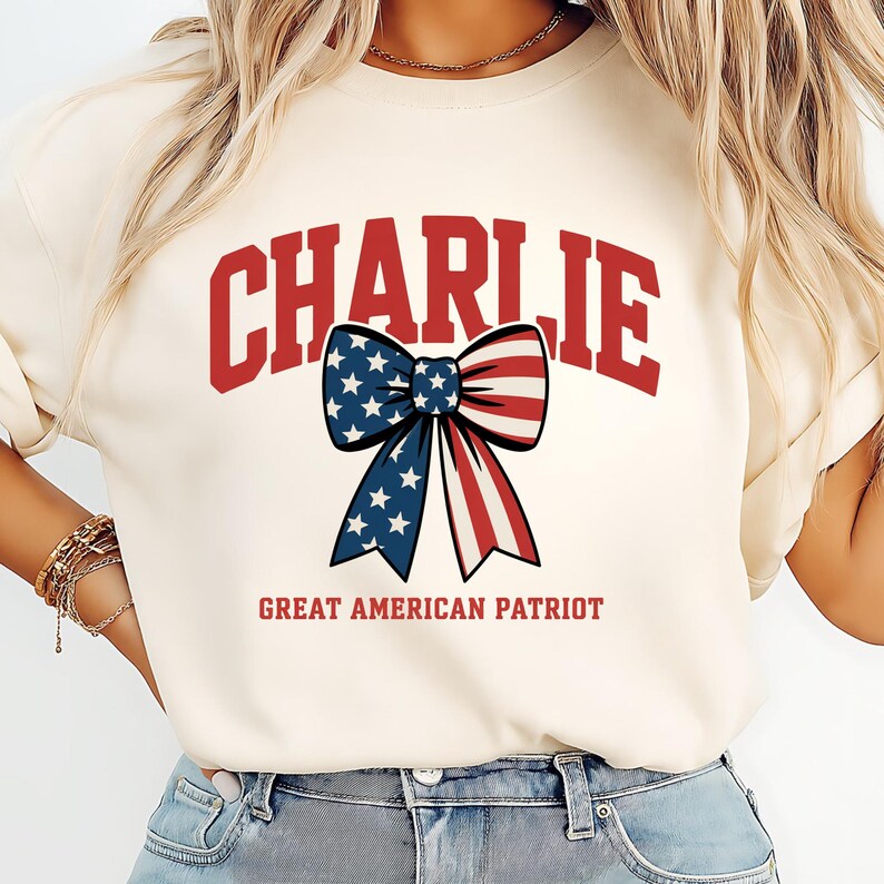 May include: Cream-colored sweatshirt with the name "CHARLIE" in red block letters. A patriotic bow graphic with blue stars and red and white stripes is centered below the name. The text "GREAT AMERICAN PATRIOT" is below the bow.