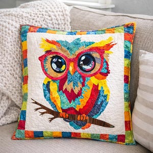 Peut inclure: Un coussin carré décoratif avec un motif de hibou coloré. Le hibou, avec de grands yeux et des lunettes rouges, est perché sur une branche. Le coussin a un fond blanc avec une bordure colorée et est placé sur un canapé gris.
