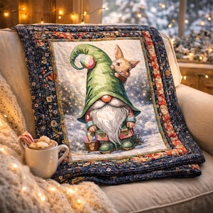 May include: A decorative quilt featuring a whimsical gnome with a long white beard and a green hat, holding a basket, and a bunny peeking out. The quilt has a floral border and is draped over a chair. A mug of hot cocoa with a candy cane sits nearby.