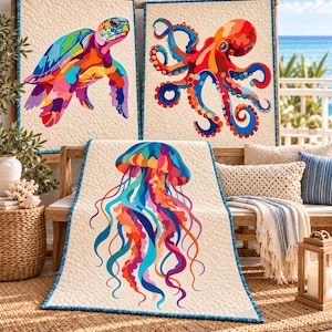 Op de afbeelding: Drie rechthoekige quilts met kleurrijke illustraties van het onderwaterleven. Eén quilt toont een zeeschildpad, een andere een octopus en de derde een kwal, allemaal op een crèmekleurige, getextureerde achtergrond met een blauwe rand.