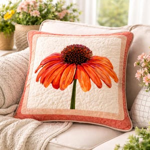 May include: Square cushion with a striking orange and red coneflower design. The flower has a dark brown centre and a green stem. The cushion has a quilted cream background and a coral border, suitable for home decoration.