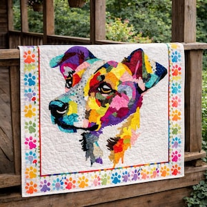 Puede incluir: Un edredón de perro colorido con un fondo blanco y un borde de huellas de patas. El retrato del perro está compuesto por varios colores, incluyendo azul, amarillo, morado y rojo. El edredón se exhibe en una barandilla de madera.