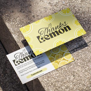 Può includere: Due biglietti di ringraziamento a tema limone. Un biglietto è giallo con le parole "Thanks Lemon" in corsivo nero e lettere maiuscole. L'altro biglietto è bianco con lo stesso testo e testo aggiuntivo sull'azienda.