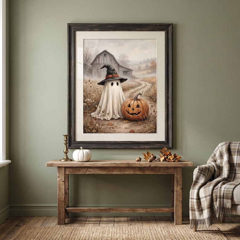 Puede incluir: Una impresi&oacute;n art&iacute;stica enmarcada que muestra a un fantasma con un sombrero de bruja negro junto a una calabaza tallada de color naranja en un camino de tierra. Al fondo, un granero r&uacute;stico se alza en un campo bajo un cielo nublado.