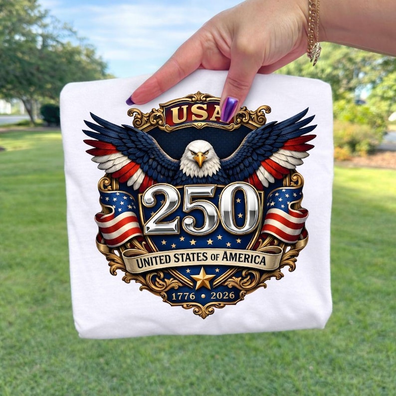 Puede incluir: Camiseta blanca con un dise&ntilde;o patri&oacute;tico para el 250 aniversario de los Estados Unidos de Am&eacute;rica. El dise&ntilde;o incluye un &aacute;guila, la bandera estadounidense y el texto "USA 250 United States of America 1776-2026".