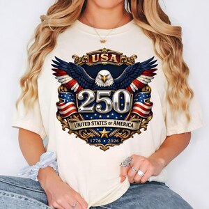 Puede incluir: Camiseta color crema con un dise&ntilde;o patri&oacute;tico que celebra el 250 aniversario de los Estados Unidos. El gr&aacute;fico incluye un &aacute;guila con las alas extendidas, el n&uacute;mero 250 y los textos "USA" y "United States of America". El dise&ntilde;o incorpora rojo, blanco y azul.