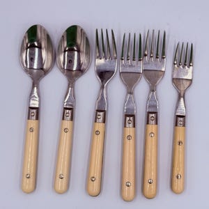 Könnte beinhalten: Ein Set aus sechs Vintage-Besteckteilen, darunter zwei Löffel und vier Gabeln. Die Löffel und Gabeln haben silberfarbene Köpfe und cremefarbene Griffe. Die Griffe sind mit kleinen, silberfarbenen Nieten befestigt. Das Besteck ist auf einer hellen Oberfläche angeordnet.