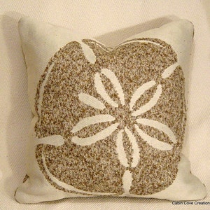 May include: A white pillow with a brown sand dollar design. The sand dollar is outlined in white and has a textured appearance.